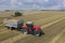 A red tractor harvests ripe golden wheat on a grain field harvested by harvesters. Agricultural work in summer.