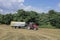 A red tractor harvests ripe golden wheat on a grain field harvested by harvesters. Agricultural work in summer.