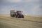 A red tractor harvests ripe golden wheat on a grain field harvested by harvesters. Agricultural work in summer.