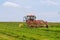 A red tractor rakes the grass to collect the silage. Agricultural machinery works on a large field