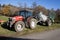 Red tractor with slurry tanker and green hoses stands on an autumn meadow, the field can be cultivated faster with these machines