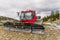 Red tractor, snow plough parked outside a mountain on the rocks