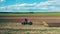 Red tractor sows seeds on plowed land.