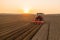 Red tractor working in agricultural field at sunset to avoid a food crisis
