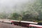 Red trains in Alishan Forest Railway stop on the platform of Zhaoping railway station with trees and fog in the background.