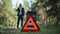 Red triangle emergency road sign on green grass with blurred young Caucasian man talking on phone at background. Sad guy