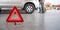 Red triangle reflector roadside warning on the floor. There is a broken pickup car in the background
