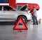 Red triangle reflector roadside warning on the floor. There is a broken pickup car in the background