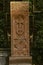 Red tuff khachkar with an arch carved with a cross, a figure of a Saint and a round symbol of eternity on the alley of stone cross