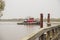 A red tug boat sailing on the Savannah River near a brown wooden pier surrounded by lush green trees with blue sky