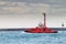 Red tugboat navigates in port waiting for a ship