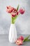 Red tulips in white vase on blue background. Still life in the style of minimalism