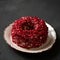 Red velvet pomegranate cake. Whole dish on clay plate. Creamy dessert decorated with red seeds or grains on black