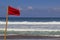 Red warning flag flapping in the wind on beach at stormy weather