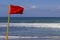 Red warning flag flapping in the wind on beach at stormy weather