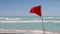 Red warning flag flutters in strong wind on a beach to alert people not to swim