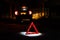 Red warning sign on the road at night in the light of a lantern against the backdrop of the dimensions of the wrecked car
