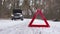 Red warning triangle on the road in front of a broken car with emergency light