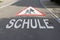 red and white attention school sign painted on concrete road. car drivers take care of pupils in traffic german text translation: