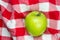 Red and white checkered table cloth with green apple