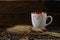 Red and white coffee cup with heart shape pattern, dry grass flowers and coffee beans on wood table