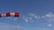 Red and white colored windsock dancing in strong wind in front of light cloudy blue sky on an airport