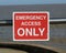 Red and white Emergency Access Only sign attached to railing in front of sea