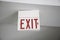 Red and white Exit sign hanging from the ceiling under the lights