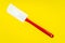 Red and white kitchen spatula made of silicone and plastic insulated on a yellow surface