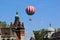 Red and white large balloon levitating with passengers high up above the city park in Budapest