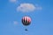 Red and white large balloon levitating with passengers high up above the city park in Budapt