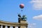 Red and white large gas filled balloon levitating with passengers high up above the city park in Budapest