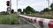 Red and white level crossing railway barrier which block the road and locomotive of empty freight train.