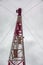 Red and white metal mobile communications tower cell site against a cloudy sky and wires. Vertical orientation.