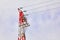 A red-white pole of a high voltage power line with wires and insulators opposite a cloudy sky. Diagonal arrangement of