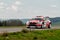 Red and white sports car driving through a winding course during a Harghita Rally race