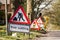 Red and white tree cutting warning signs standing at side of road with road works worker symbol. Traffic sign alerting drivers.