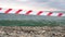 Red white warning tape barrier ribbon swinging in the wind across exotic sea beach background without people. No entry