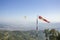 A red white windsock on the background of a flying paraglider in a clear blue sky and green mountains with a city in the valley