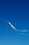 Red and white windsock on a pole with blue sky in background