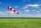 Red and white windsock wind sock on blue sky, green field and clouds background on aerodrome or airdrome. Shows wind speed and