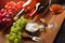 Red and white wine bottles with bunch of grapes, cheese head, nuts and wineglass on wooden board and black background