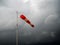 Red windsock on black stormy sky. Bad weather, meterological wind indicator.