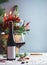 Red wine bottle and wineglass on table with Christmas decoration, candles, snow and fir branches at blue wall background. Festive