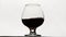 Red wine forms beautiful wave. Alcohol drink pouring in wine glass over white background. Close-up shot. Slow motion of
