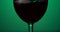Red wine forms beautiful wave. Wine pouring in wine glass over green background. Close-up shot.