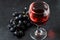 Red wine in a glass, a bunch of grapes. Dark background