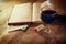 Red wine glass and old book on wooden table at sunset burst. vintage filtered image