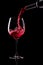 Red wine pouring into glass isolated on black background. Rose wine splashing in glassware.