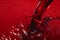 Red wine pouring with splashes on red background closeup. Glass of wine, drink for celebrating, date, family dinner, party. Wine